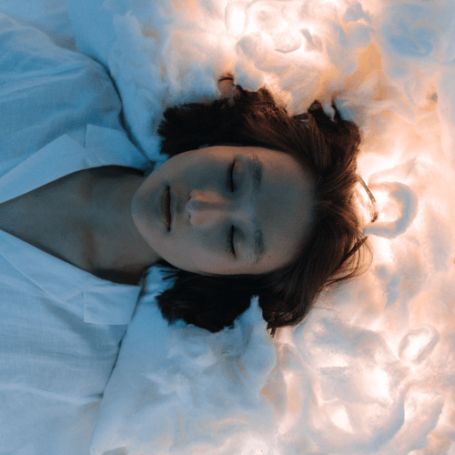 A woman peacefully sleeping with a lighted background that suggests dreaming